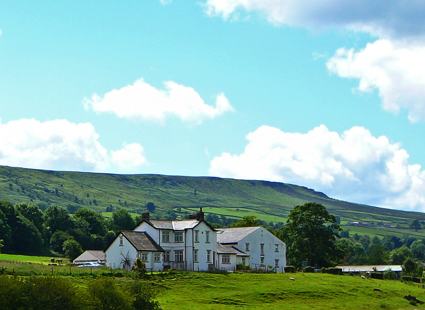Hadfield Farm's white farmhouse on green pasture with the open slope of the moor rising behind